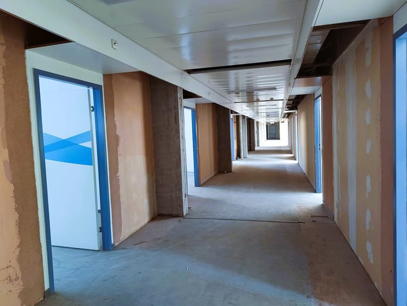 Empty corridor with closed doors, beige walls, and white ceiling