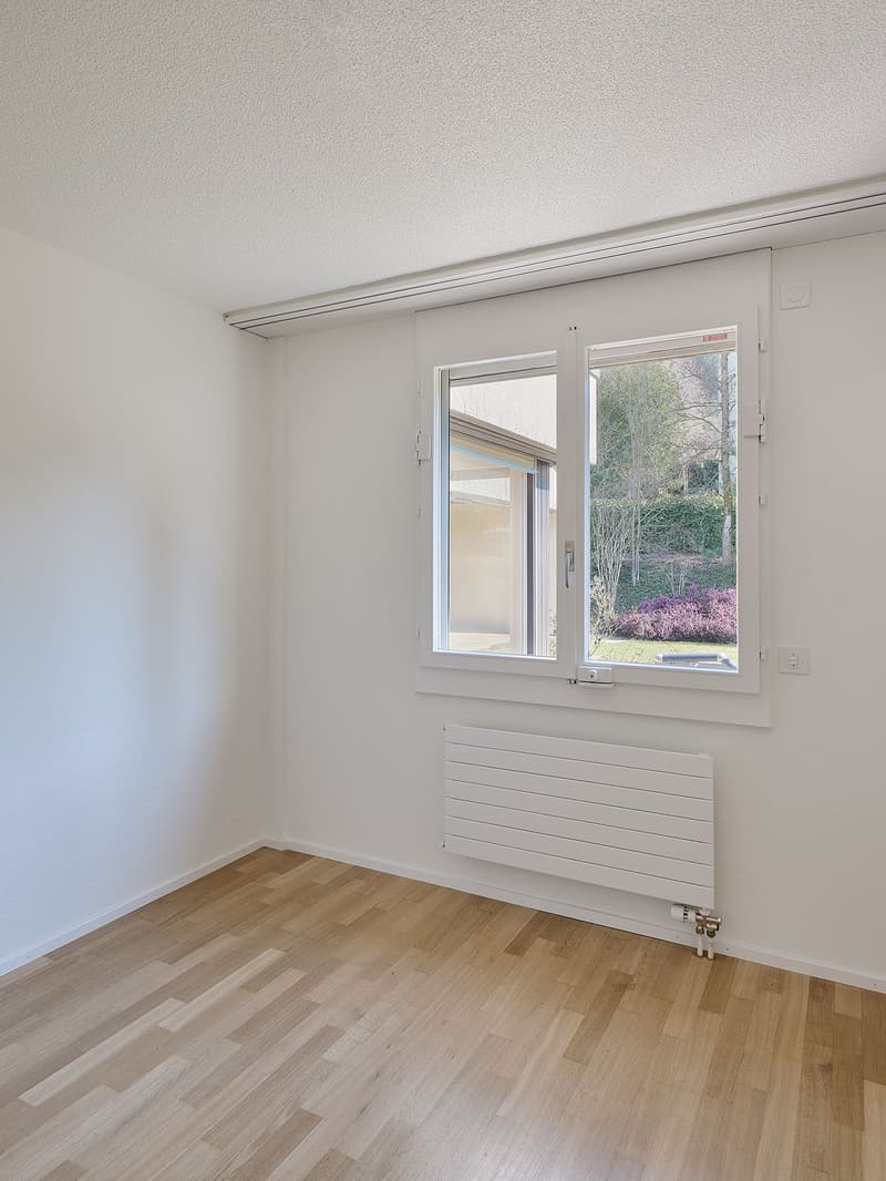 empty room with wooden floor, white walls, large window with shutters, heater