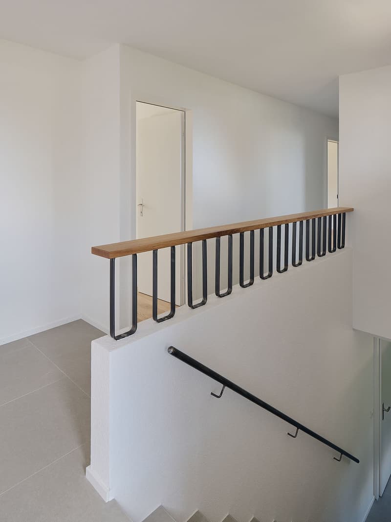 white walls, wooden handrail, black metal railing, light gray flooring