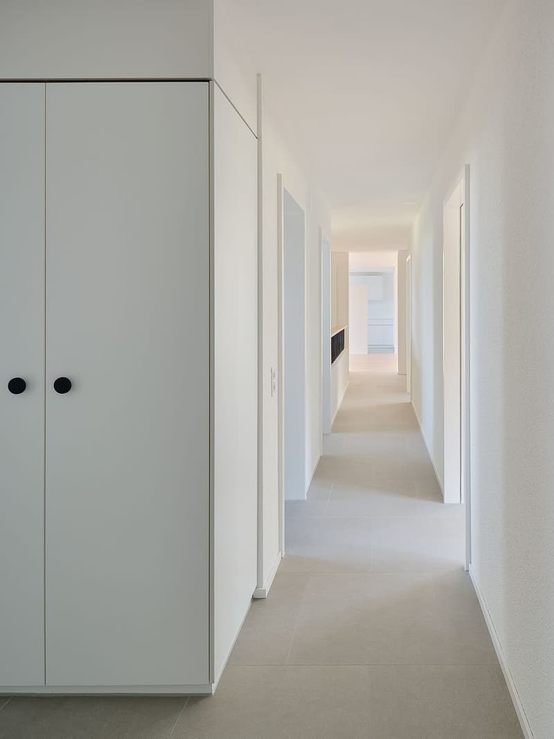 white hallway with built in storage on the left, and rooms on the right, beige tile flooring