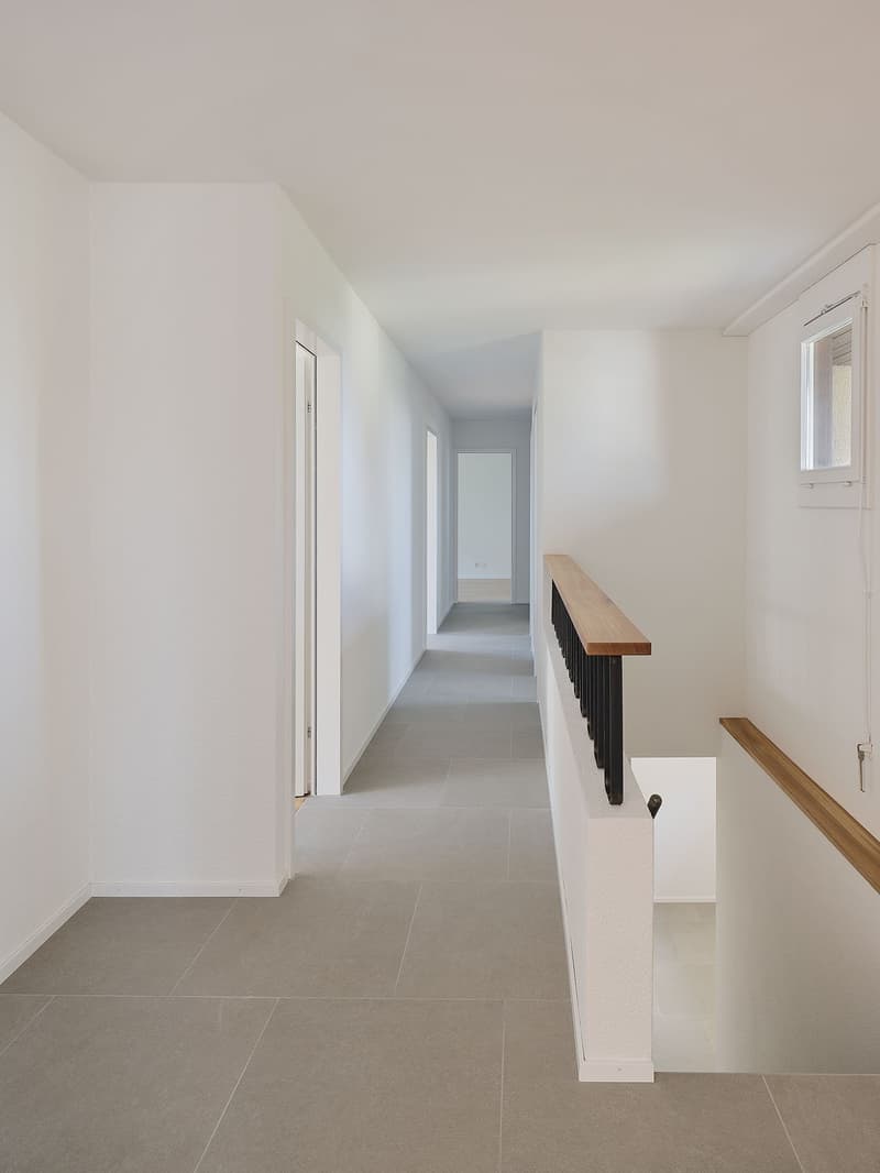 Empty hallway, white walls, grey floor, wooden handrail