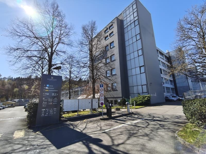 High-rise building, glass windows, parking lot, trees, street sign, bushes, cars parked