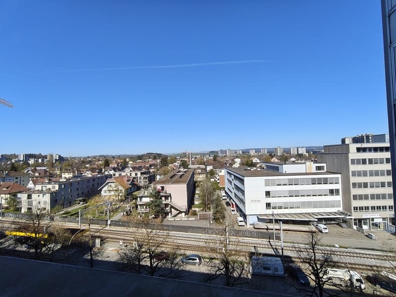 Aerial view of a city with multiple buildings, a railway track, and a clear blue sky.