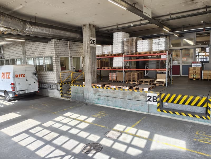 Warehouse with a white van parked, shelves with boxes, concrete floor, yellow markings, and a staircase
