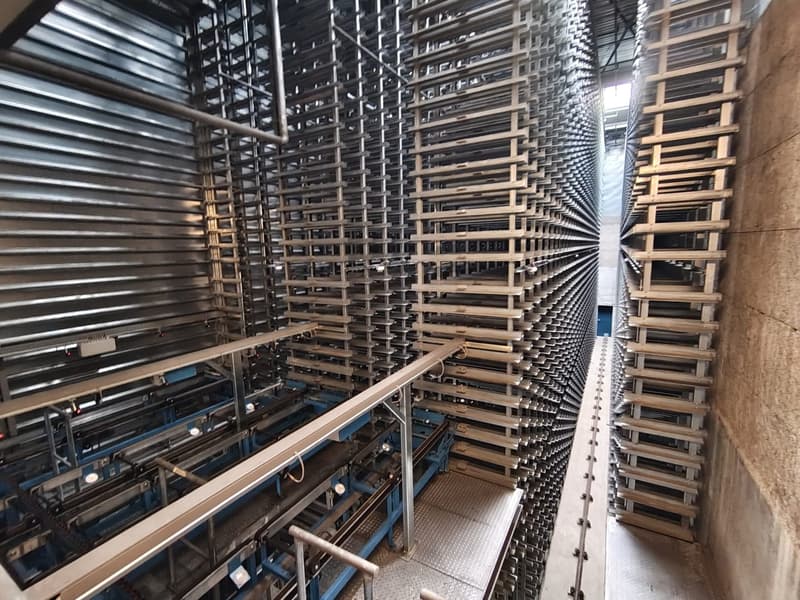 Industrial facility with multiple levels of metal shelving units, metal beams, and a conveyor system.