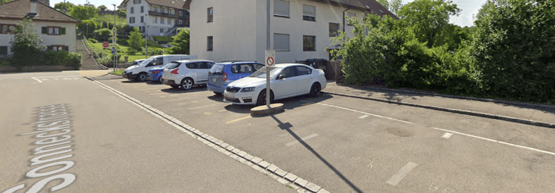Parking area with multiple cars parked in front of a building with multiple floors and windows.