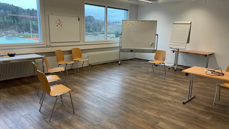 empty room with wooden floor, white walls, whiteboards, radiators, tables, chairs