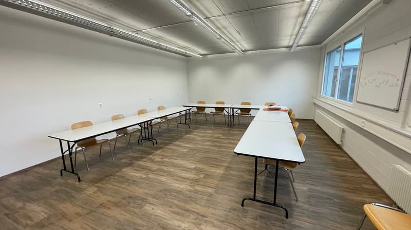 empty room with white walls, wooden floor, long tables, chairs, whiteboard, windows, radiators