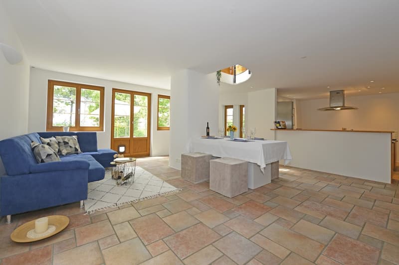 L-shaped blue sofa, white dining table, white rug, wooden floors, windows, potted plant, wine bottle, candles, wine glasses