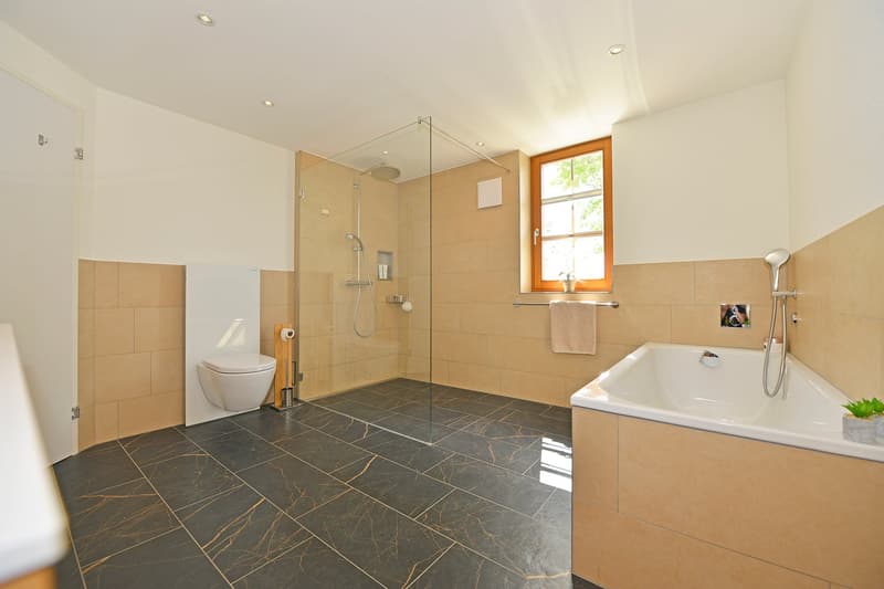 Modern bathroom with walk-in shower, toilet, bathtub, and window. Tiled floor, beige walls, and fixtures.
