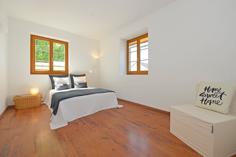 Bed, 2 windows, hardwood floors, decorative pillows, small side table with lamp, bench