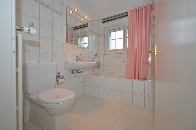 Modern, clean bathroom with white ceramic tiles, shower, bathtub, white sink, mirror, toilet, and a pink shower curtain