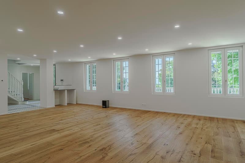 spacious room with wooden floors, white walls, large windows, and mounted lights
