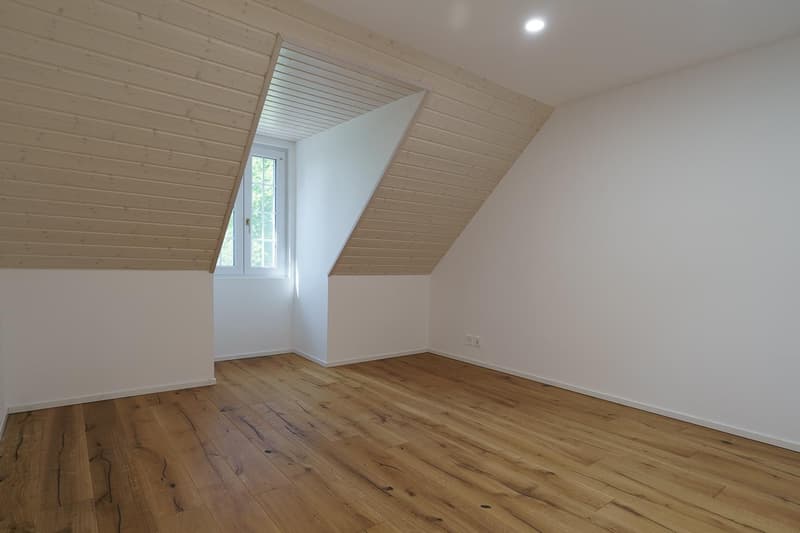 empty attic room with slanted ceilings, wooden floor, small window