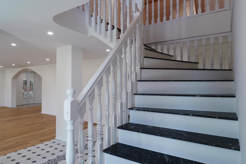 Modern design staircase with marble steps, wooden ceiling, white railings, polished wooden floor.