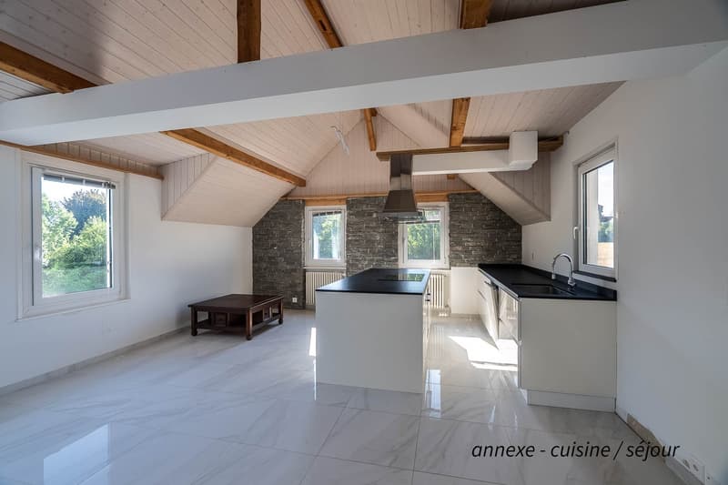 white marble tiles, kitchen island with black countertops, sink with faucet, wooden table, white ceiling with wooden beams, white walls, windows, modern design