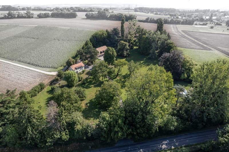 Aerial view of countryside with house and driveway, surrounded by green trees and farmland.