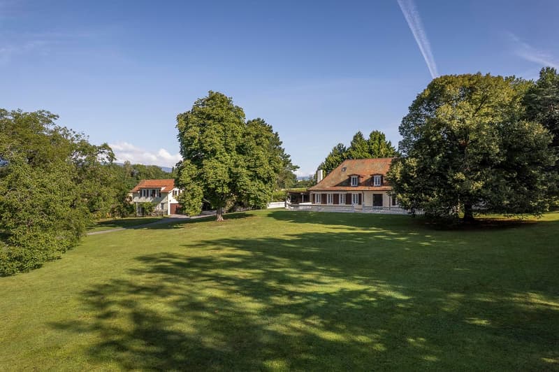 Large two-story house in the middle of a big grass field with trees, wide driveway