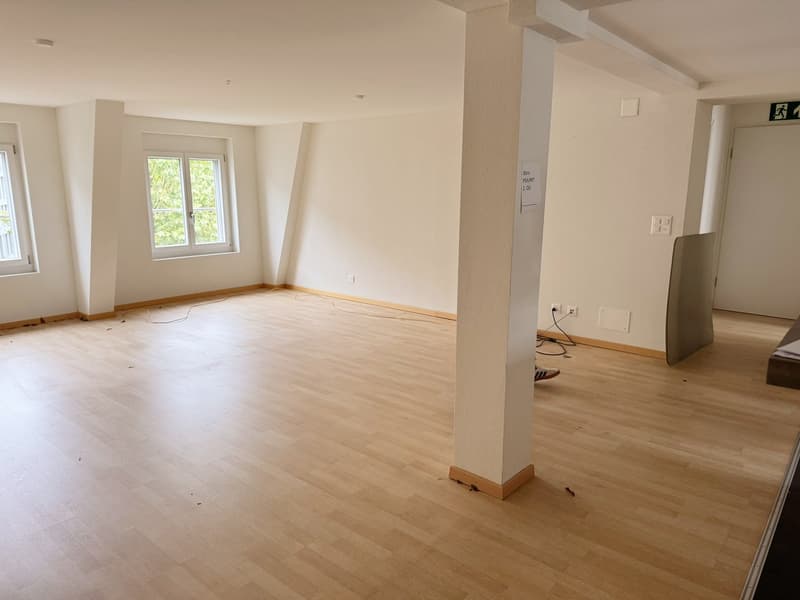 large room, white walls, wooden floor, windows, central pillar