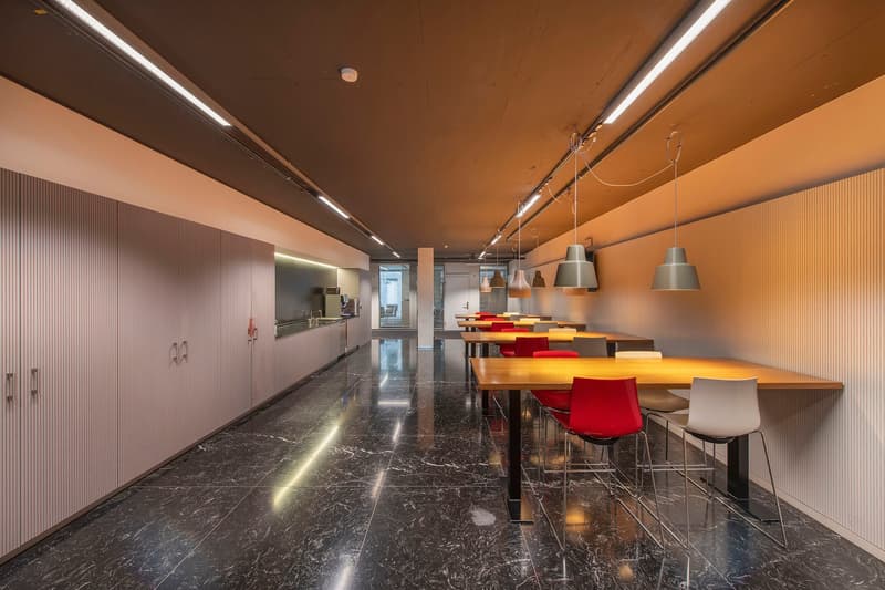 marble floor, long wooden tables, red and white chairs, hanging lamps, cabinets, kitchen area