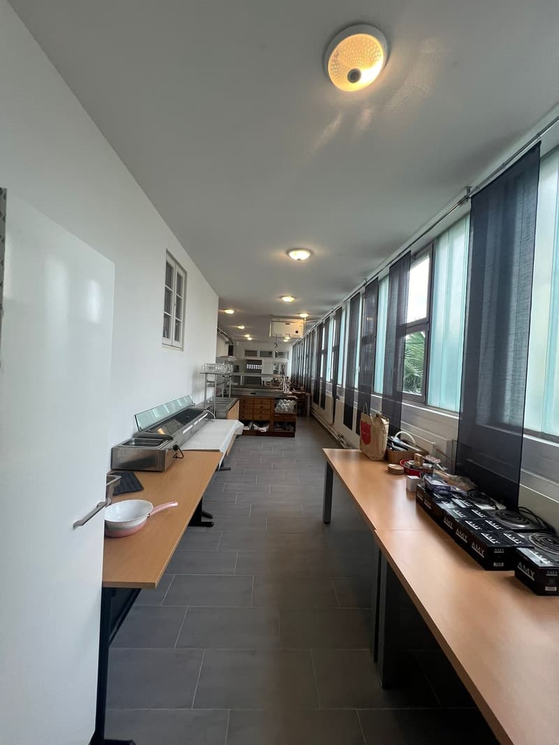 Dining area, white walls, tiled floor, long wooden tables, stainless steel appliances, wooden cabinets, several windows with black curtains