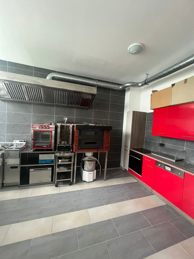Commercial kitchen with ovens, kitchen cabinets, dishwasher, microwave, gas stove, tiled floor, and steel kitchen carts