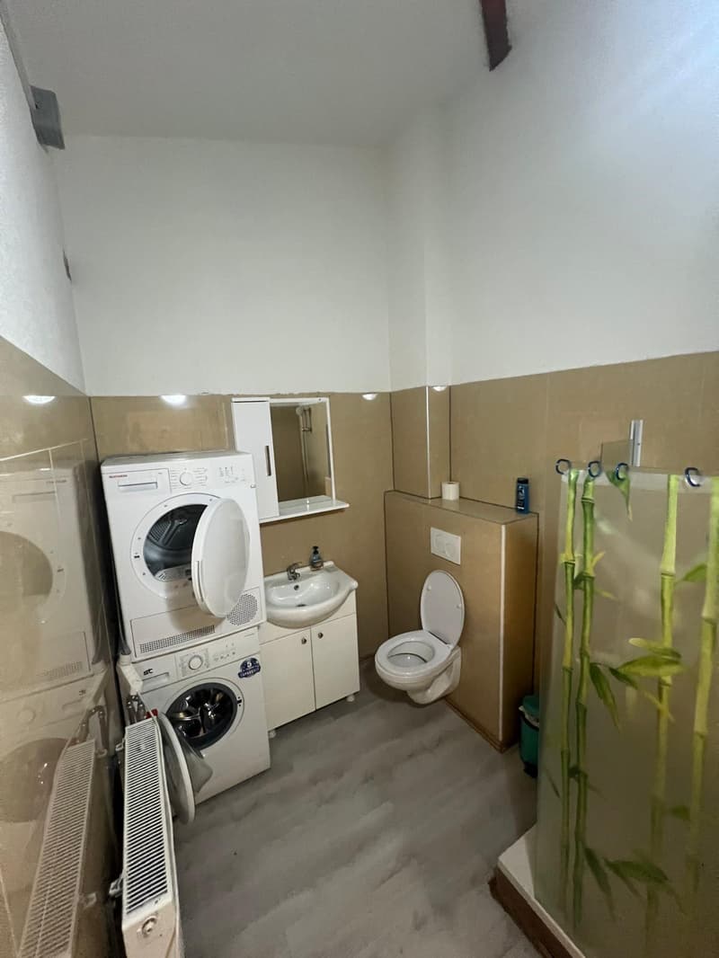 A compact bathroom with a washing machine, a sink, a toilet, and a shower. Tiled walls and flooring.