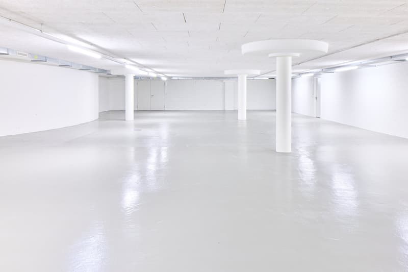 Large open-plan commercial space with white walls, white ceiling, and white concrete floor. The space has several white columns supporting the ceiling and appears to be a vacant office or studio space.