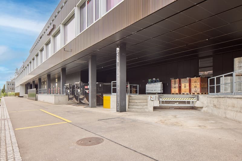 Large industrial building with loading docks, storage containers, and a parking area in front
