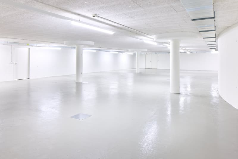 Large open floor plan with white walls, concrete floor, and fluorescent lighting. The space appears to be a commercial or industrial building, possibly a warehouse or office space. There are no visible features from the provided list.