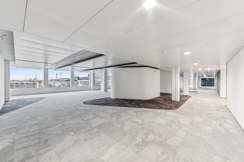 large open space, white walls, gray flooring, central column, glass windows with city view