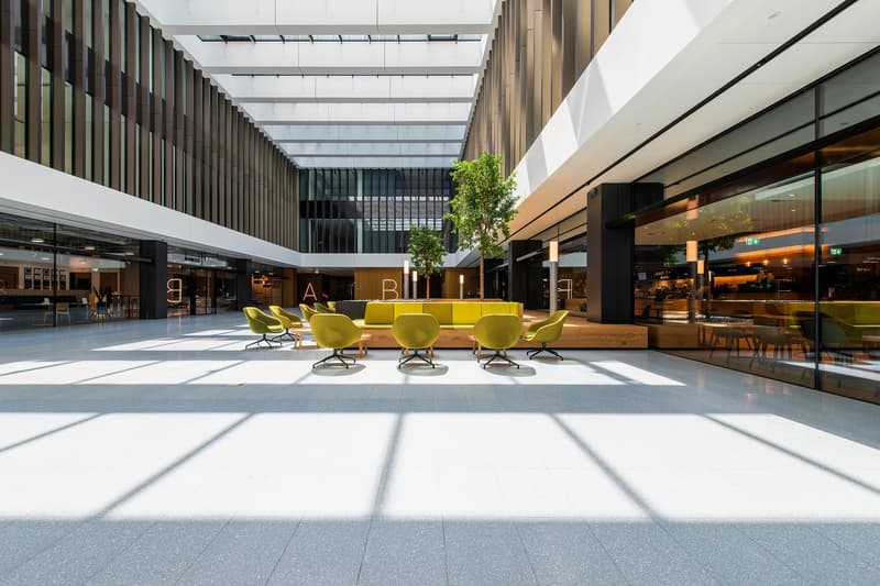 Open lobby with modern furniture, glass partitions, seating areas, trees, and ample natural light.