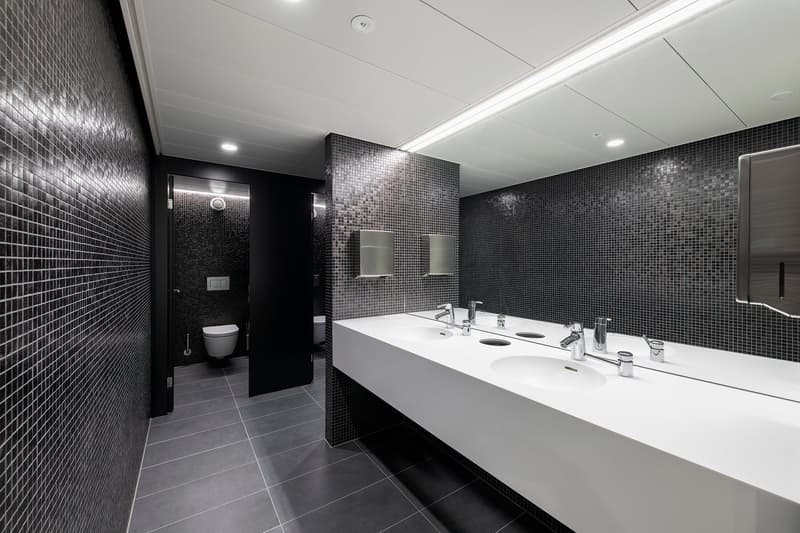 modern, minimalistic bathroom with black and white tiled walls, grey floor, dual sinks, mirrors, and a toilet in a partitioned area