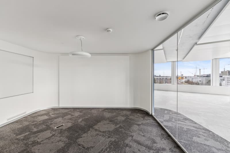Contemporary minimalist design, large glass windows, gray carpeting, ceiling light fixture, blank whiteboard, curved corners