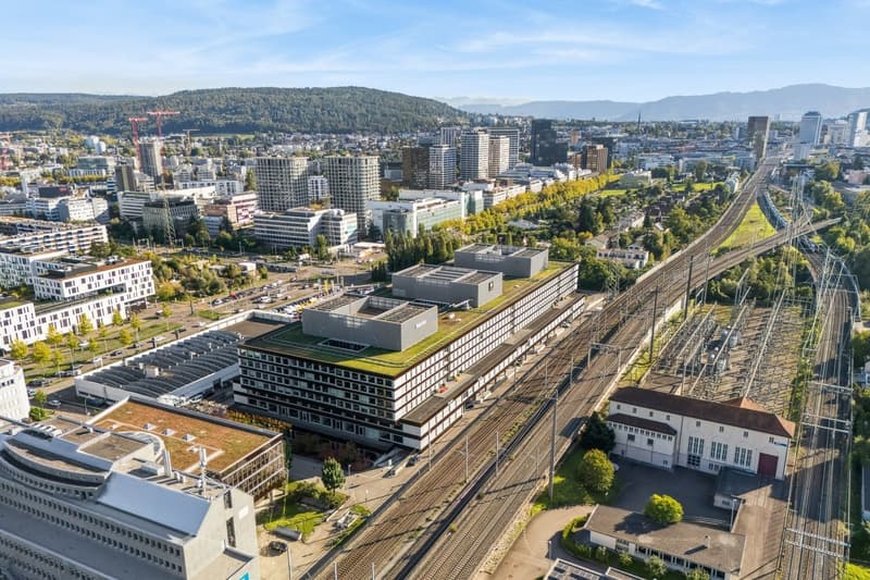 Urban area with numerous buildings, railway tracks, greenery, mountain range in the distance
