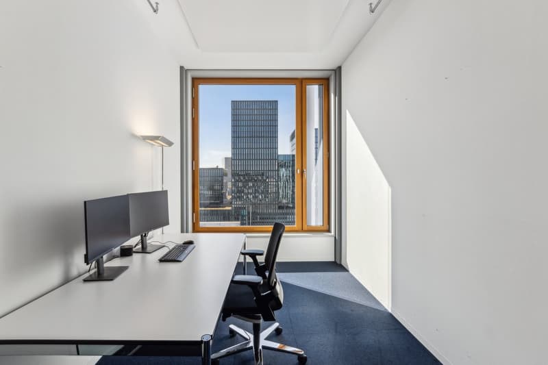 Spacious office with large window overlooking a modern city skyline, a desk with a computer setup, and a comfortable office chair.