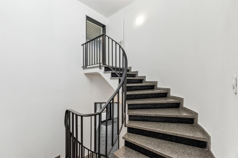 Spiral staircase with granite steps and black metal railing leading to a balcony or upper level