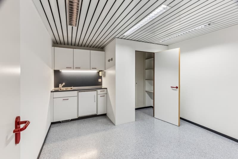 Compact studio apartment with kitchenette, white cabinets, dishwasher, and open doorway leading to another room