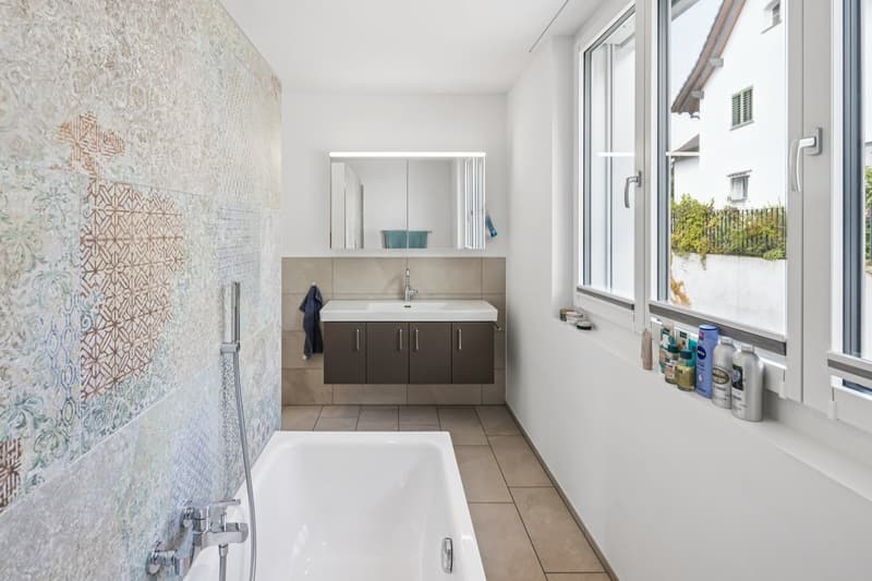 Modern bathroom with bathtub, sink, mirror, and window