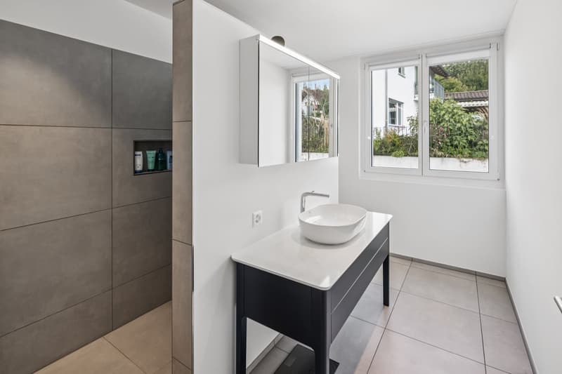 minimalistic design with white tile flooring, white sink with a faucet, a white mirror, shower stall with tiled walls, natural light from a large window