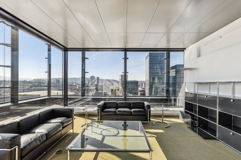 modern living room with leather couches, glass coffee table, and large windows