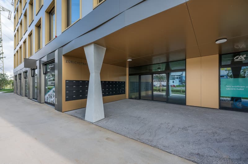 Modern building with glass doors, concrete column, mailboxes, and a paved entrance area.