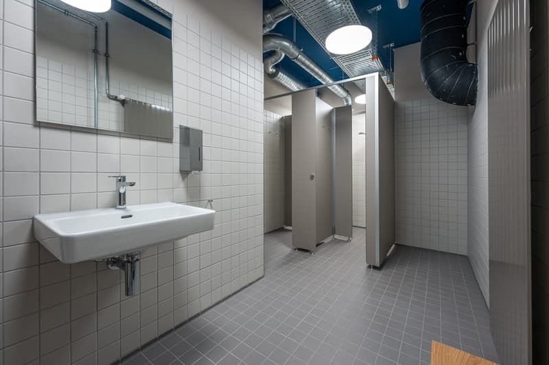 Bathroom with white tiles, sink, mirror, and toilet stalls