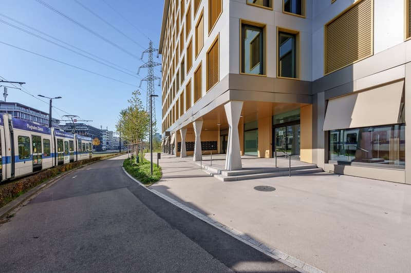 Modern building with white and yellow exterior, multiple windows, entrance with steps, tram tracks nearby