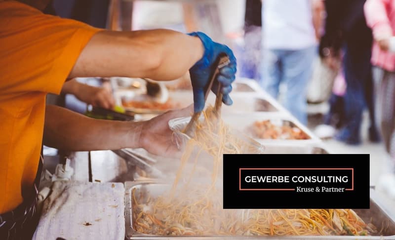 A person in an orange shirt and blue gloves is preparing food in a buffet line.