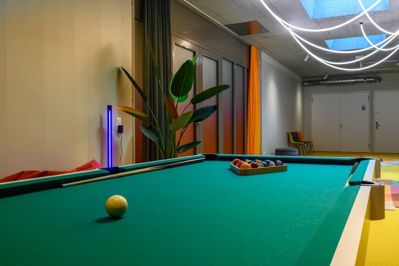 Green pool table with billiard ball and pool stick, potted plant, blue lights, yellow floor