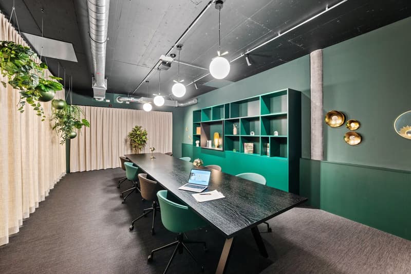 modern meeting room with a long desk and swivel chairs, green shelves with decorative items, hanging plants, and lamps
