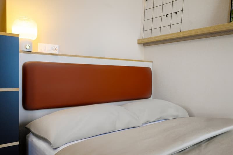 Bed with orange headboard, two white pillows, white bedding, lamp on headboard, blue cabinet on left