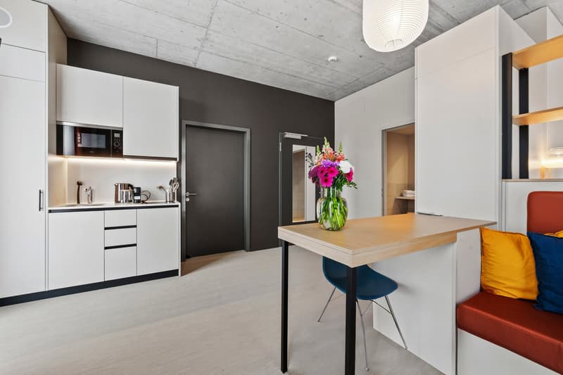 Minimalist kitchen with kitchen island, modern decor, black microwave, silver coffee maker, faucet, white cabinets, wooden table, blue chair, and a red couch with pillows