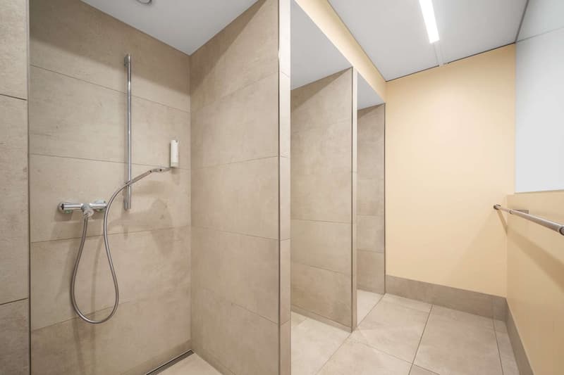 Large, modern bathroom with beige tile walls and floors, a glass-enclosed shower with a rainfall showerhead, and a towel rack.